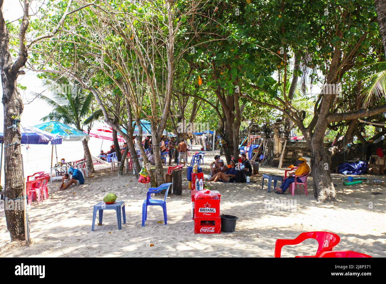 Strandszene am Kuta Beach in Bali, Indonesien, mit lokalen Händlern, die im Schatten unter den Bäumen sitzen und nur wenige, wenn überhaupt, Touristen im Jahr 2022. Stockfoto