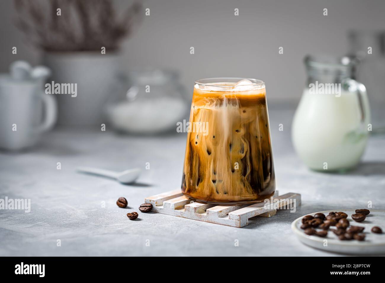 Eiskaffee in einem transparenten Glas mit Eis und Milch auf grauem Hintergrund. Stockfoto