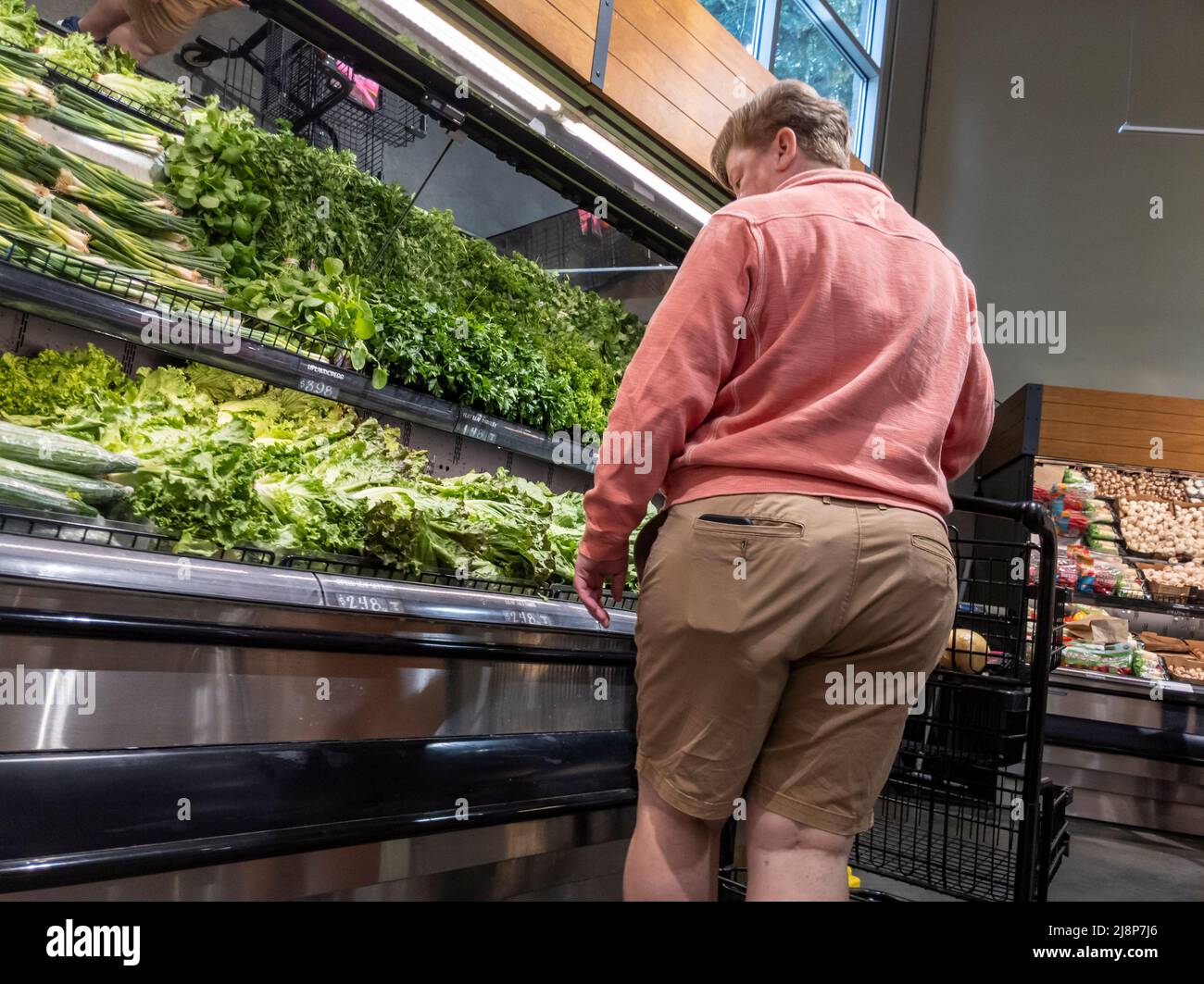Mill Creek, WA USA - ca. Mai 2022: Schräge Ansicht einer Person, die in der Produktionsabteilung eines Town and Country-Lebensmittelladens Gemüse kauft Stockfoto