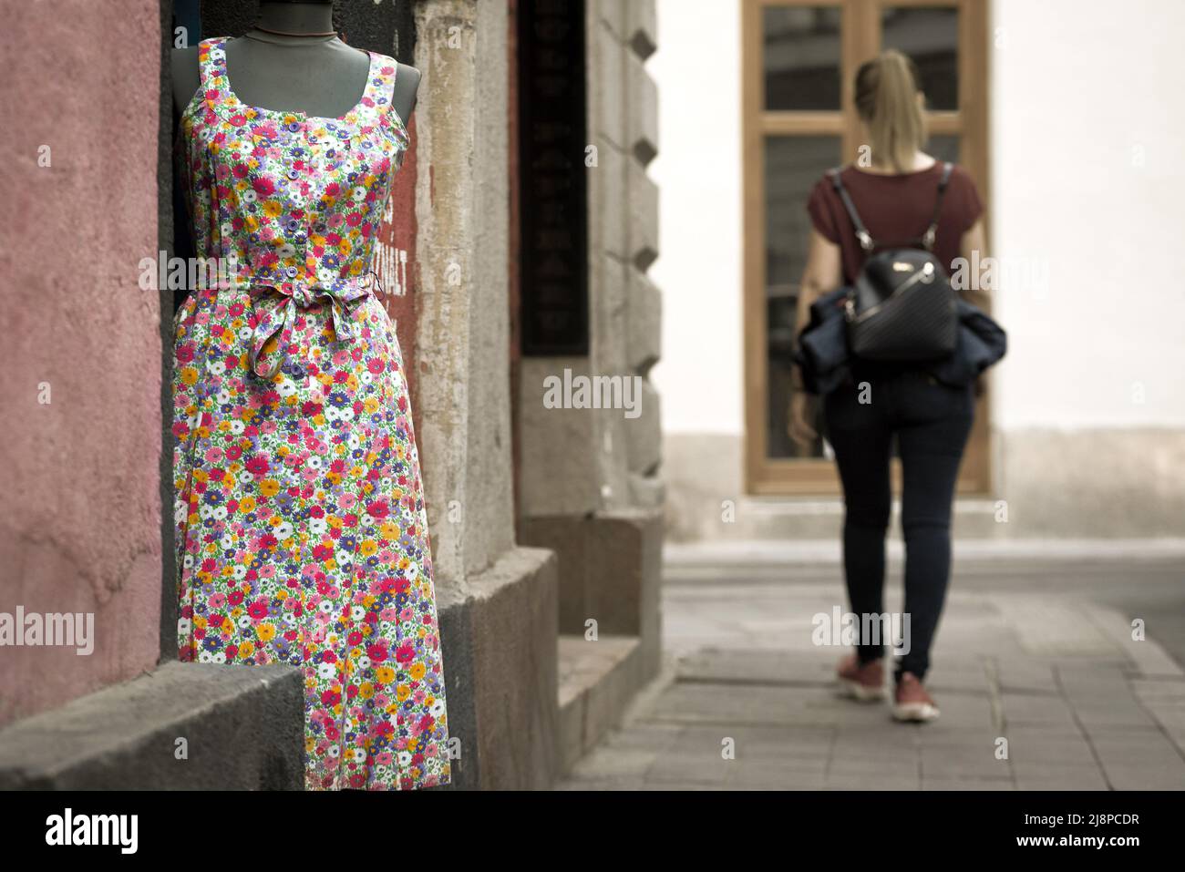 Frau in T-Shirt und Jeans, die an einem Kleid vorbeikommt, das in einem Geschäft ausgestellt ist Stockfoto
