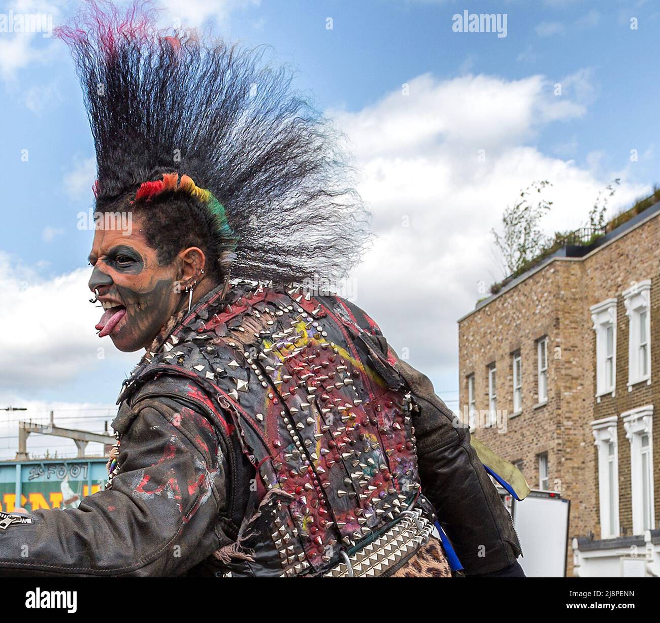 Ein Punk-Rocker mit einer fantastischen Mohawk-Frisur, gespaltener Zunge, Gesichts-Tattoos und Piercings schlägt eine wütende Pose auf der Straße. Stockfoto