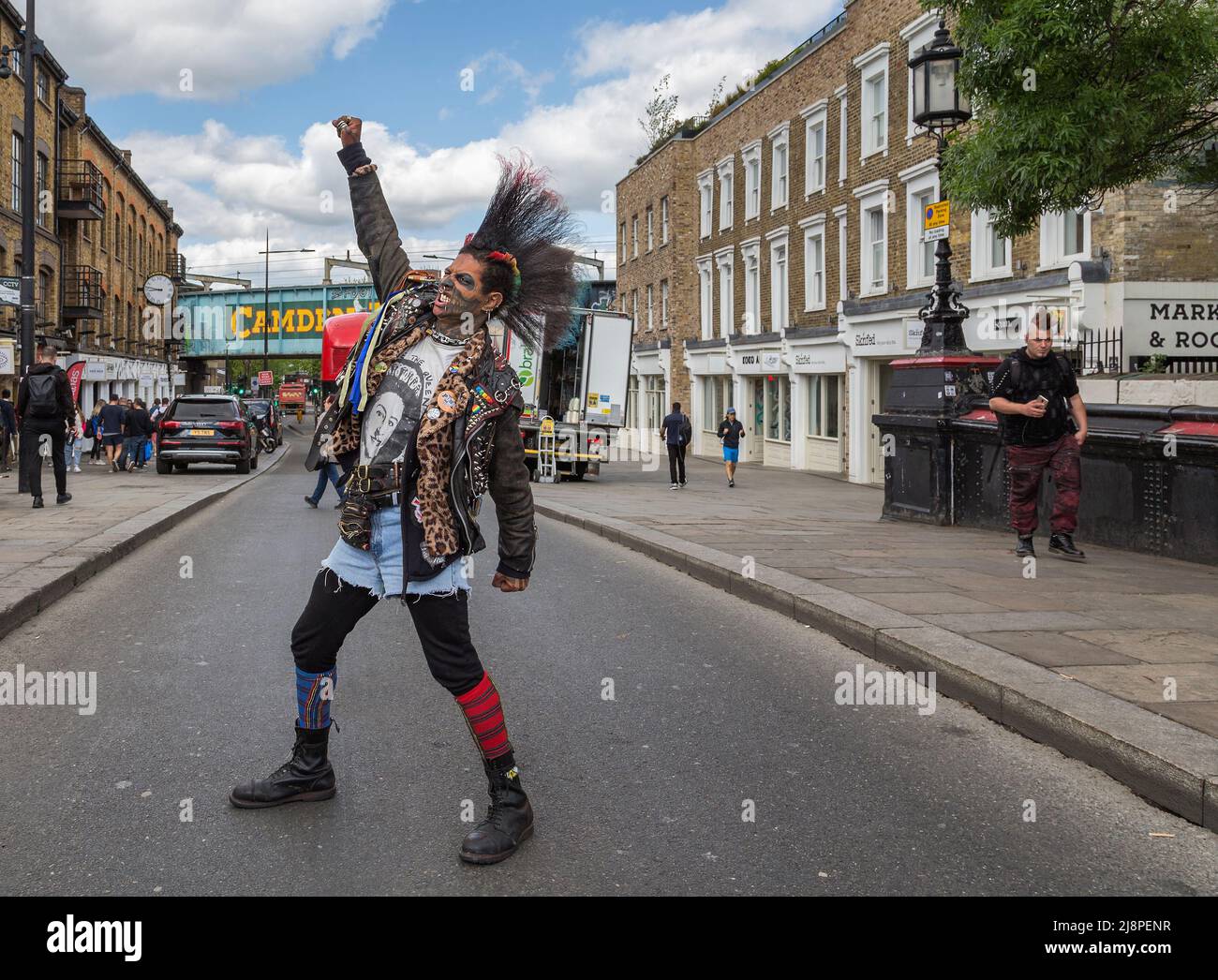 Ein Punk-Rocker mit einer fantastischen Mohawk-Frisur, der mitten auf der Straße steht, eine geballte Faust hebt und durch gerissene Zähne knurrst Stockfoto
