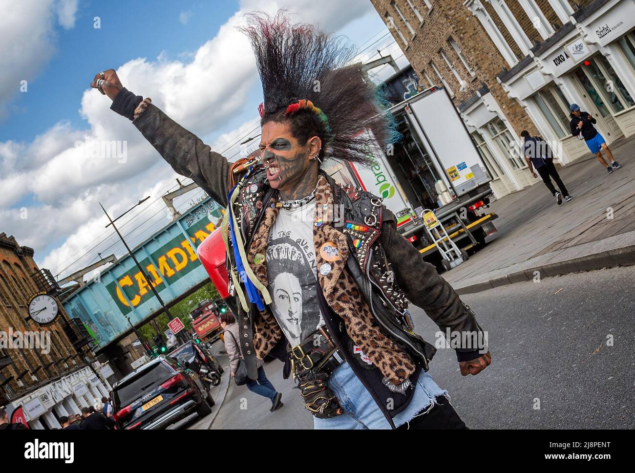 Ein Punk-Rocker mit einer fantastischen Mohawk-Frisur, der eine geballte Faust hebt und durch gerissene Zähne knurbelt, während er mitten auf der Straße steht, Stockfoto