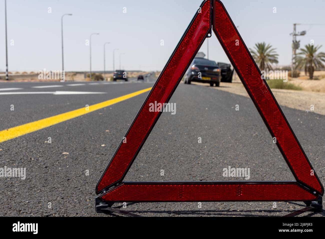 Rotes Warndreieck für Notfälle auf dem Straßenschild mit der gelben Straßenlinie und dem schwarzen kaputten Auto Stockfoto