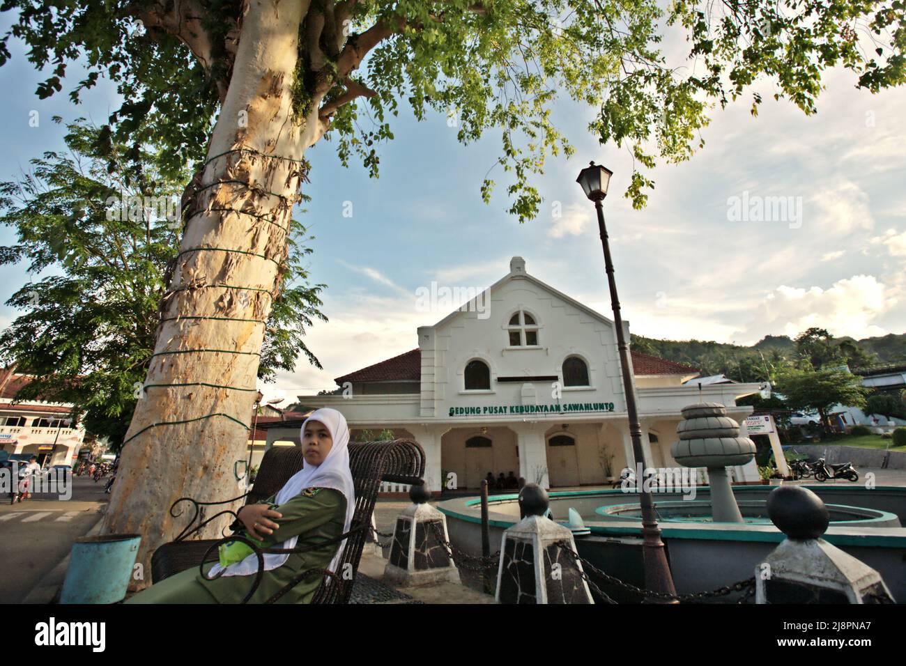 Eine Frau in Regierungsuniform sitzt auf einer Bank im Hintergrund von Gedung Pusat Kebudayaan Sawahlunto (Sawahlunto-Kulturzentrum) in Sawahlunto, einer ehemaligen Kohlebergbaustadt, die Ende des 19.. Jahrhunderts von niederländischen Kolonialisten in West-Sumatra, Indonesien, gegründet wurde. Stockfoto