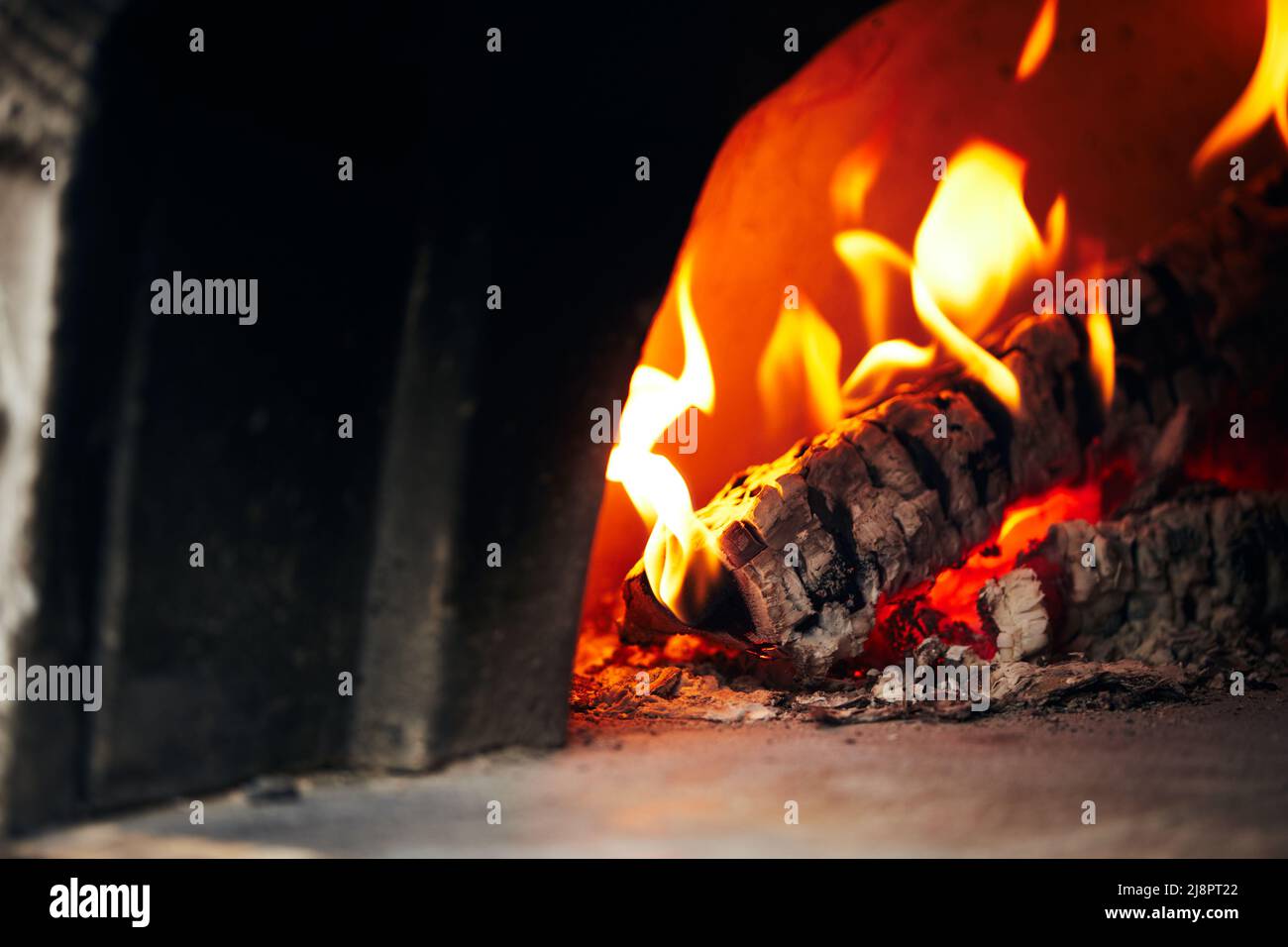 Holzofen mit Birkenstämmen zum Anzünden. Das Feuer brennt und der Ofen heizt sich auf. Vorderansicht. Stockfoto