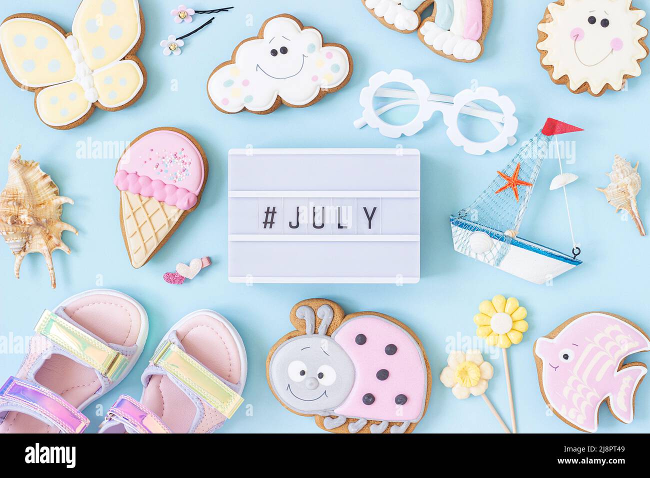 Juli-Text auf Leuchtkasten und niedliche Sommer-Symbole auf blauem Hintergrund. Draufsicht, Flat Lay. Kreatives Sommerkonzept, Grußkarte. Stockfoto