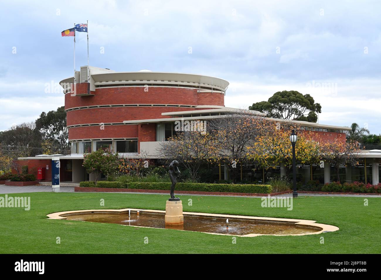 Garten mit Rasen, einem flachen Pool und Skulpturen, neben der kreisförmigen Bayside Council Chamber und der Brighton Library, beide im Hintergrund Stockfoto
