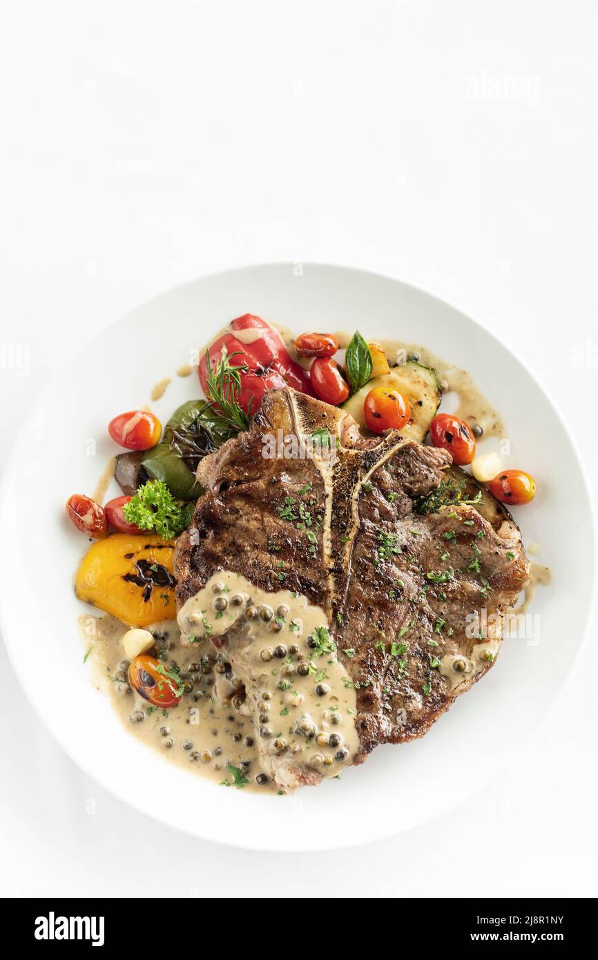 Gegrilltes T-Bone-Steak mit Pfeffercornsoße und Gemüse auf weißem Hintergrund Stockfoto