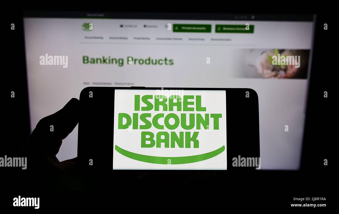 Person, die ein Mobiltelefon mit dem Logo der Firma Israel Discount Bank Ltd. (IDB) auf dem Bildschirm vor der Business-Webseite hält. Konzentrieren Sie sich auf die Telefonanzeige. Stockfoto