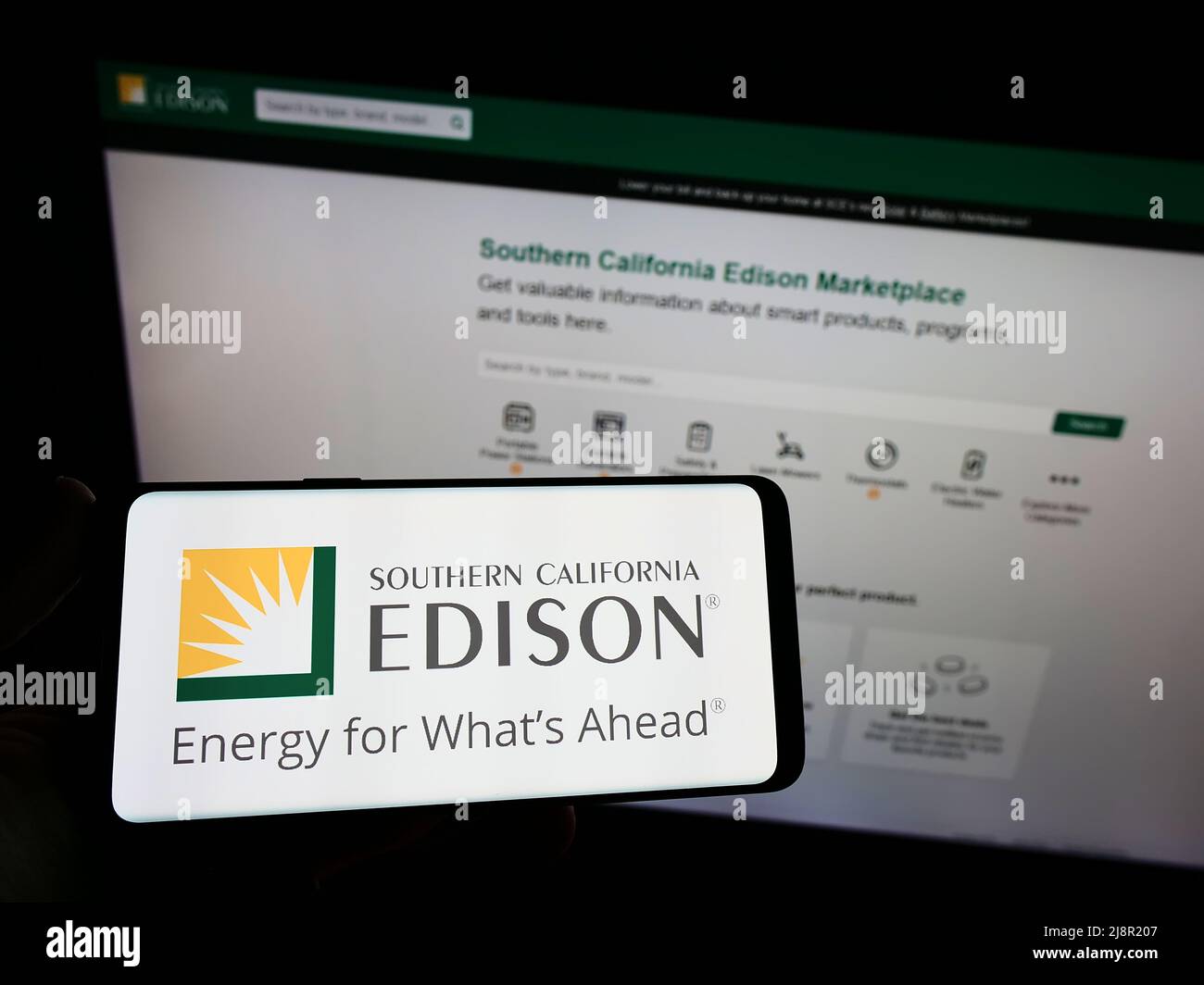 Person, die das Smartphone mit dem Logo des US-amerikanischen Unternehmens Southern California Edison (SCE) auf dem Bildschirm vor der Website hält. Konzentrieren Sie sich auf die Telefonanzeige. Stockfoto
