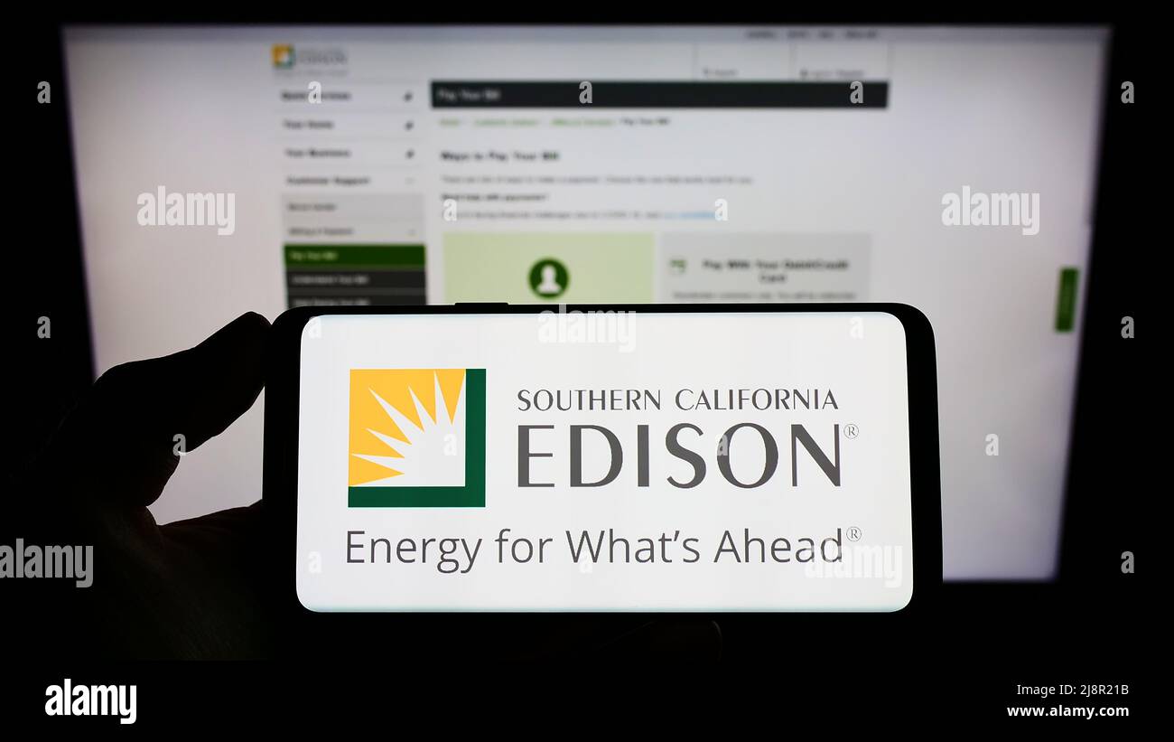 Person, die das Mobiltelefon mit dem Logo des amerikanischen Unternehmens Southern California Edison (SCE) auf dem Bildschirm vor der Webseite hält. Konzentrieren Sie sich auf die Telefonanzeige. Stockfoto