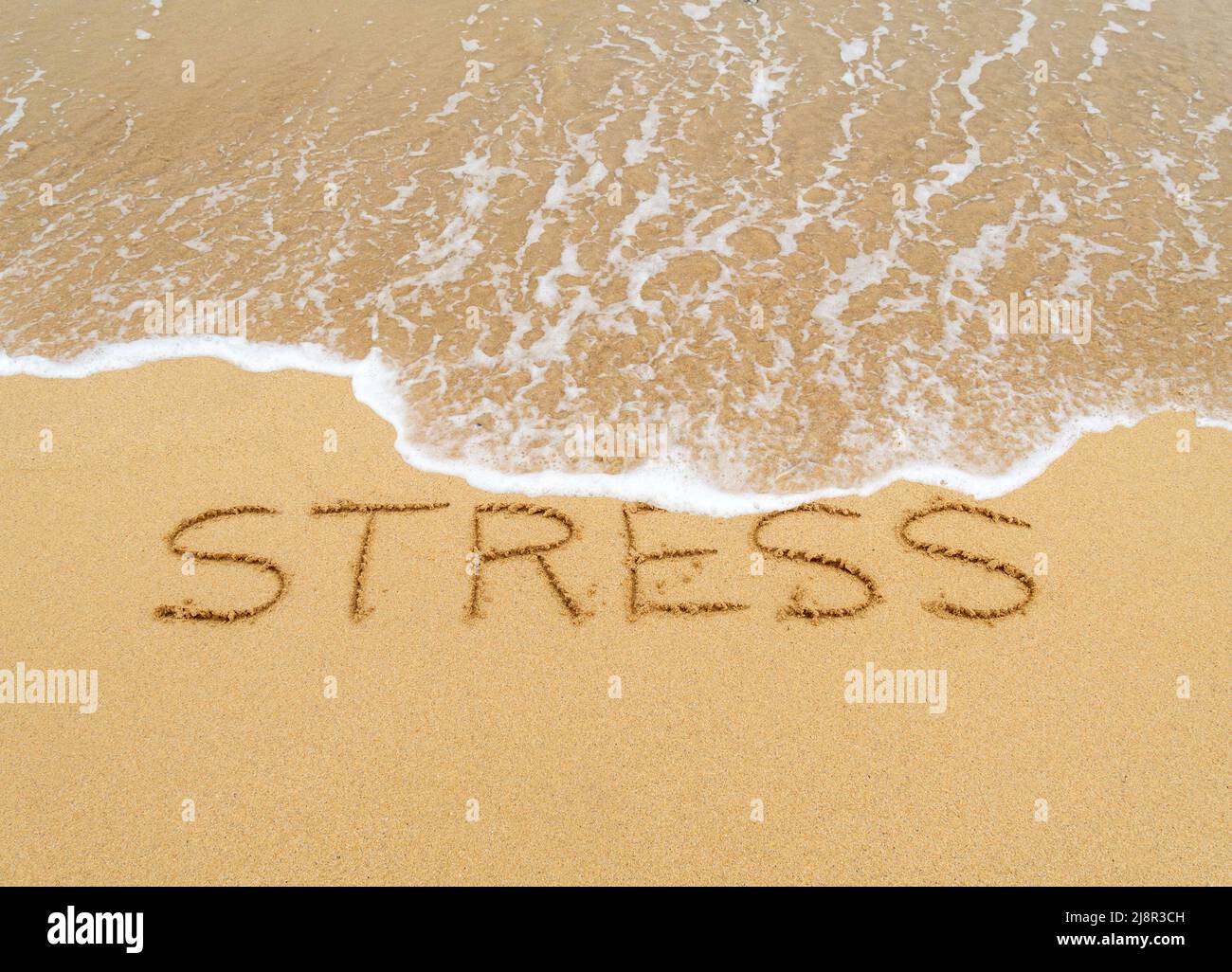 Konzeptbild - um den Stress abzuwaschen, indem man einen Urlaub macht, während die Wellen an einem Sandstrand das Wort „Stress“, das in Sand geschrieben ist, wegspülen. Stockfoto