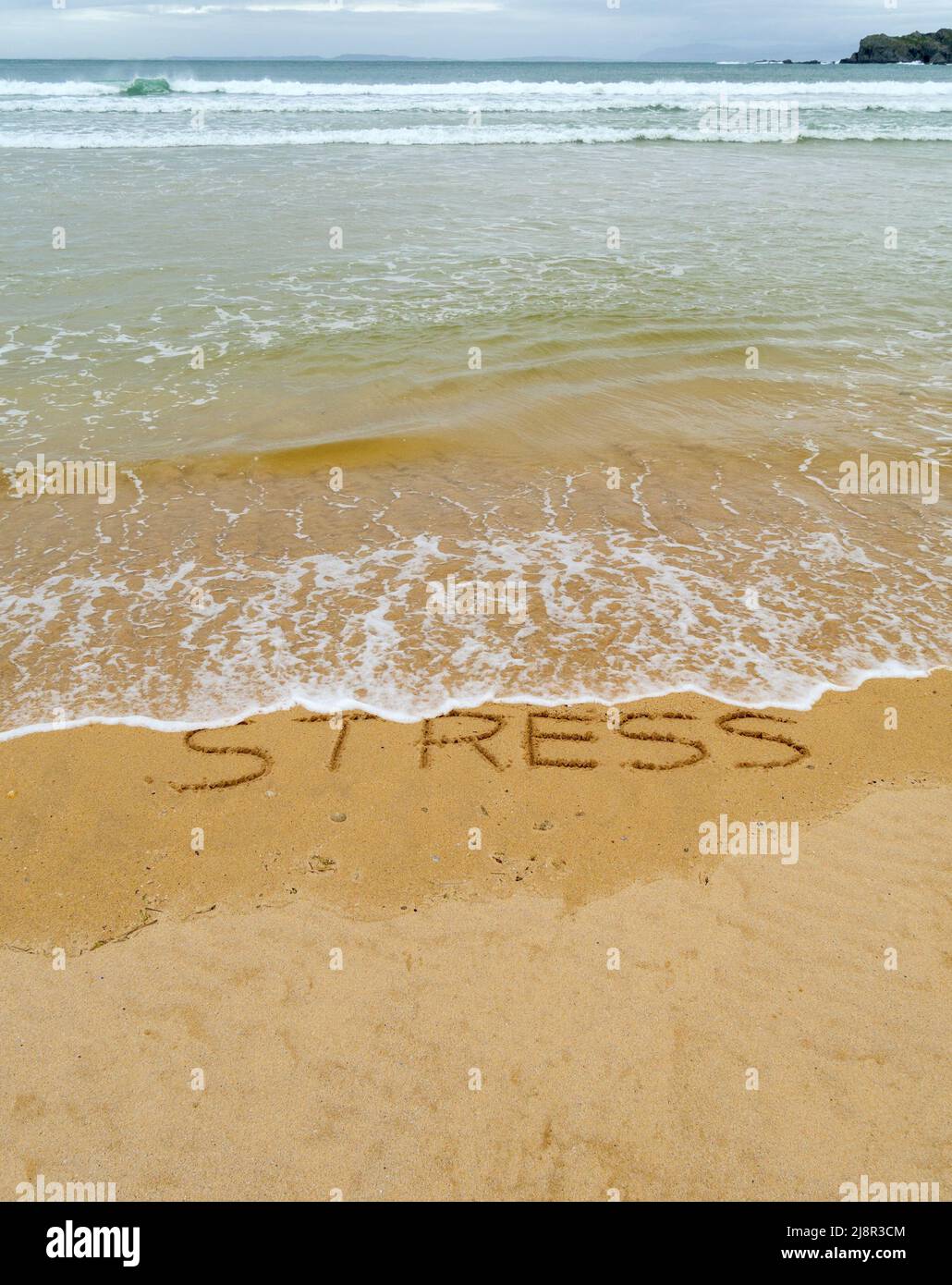 Konzeptbild - um den Stress abzuwaschen, indem man einen Urlaub macht, während die Wellen an einem Sandstrand das Wort „Stress“, das in Sand geschrieben ist, wegspülen. Stockfoto