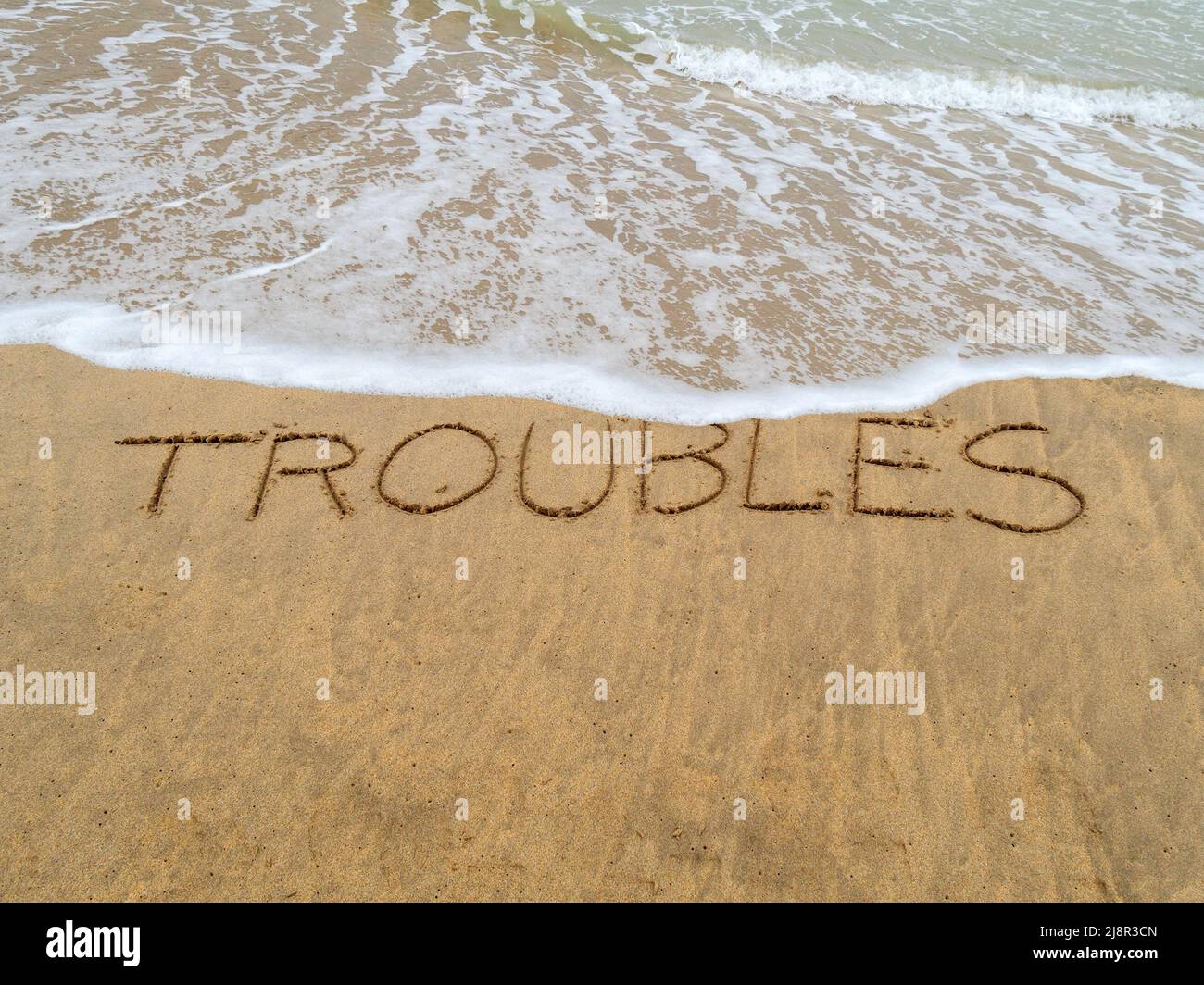 Konzeptbild - um Stress abzuwaschen, indem man einen Urlaub macht, während die Wellen an einem Sandstrand das Wort „Probleme“, das in Sand geschrieben ist, wegspülen. Stockfoto