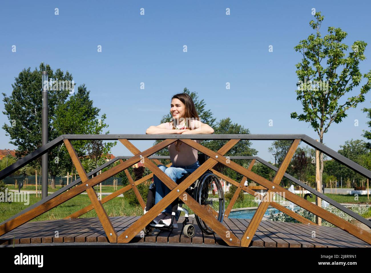 Porträt einer gelähmten Frau im Rollstuhl, die lächelt und allein im Park einen sonnigen Tag genießt Stockfoto