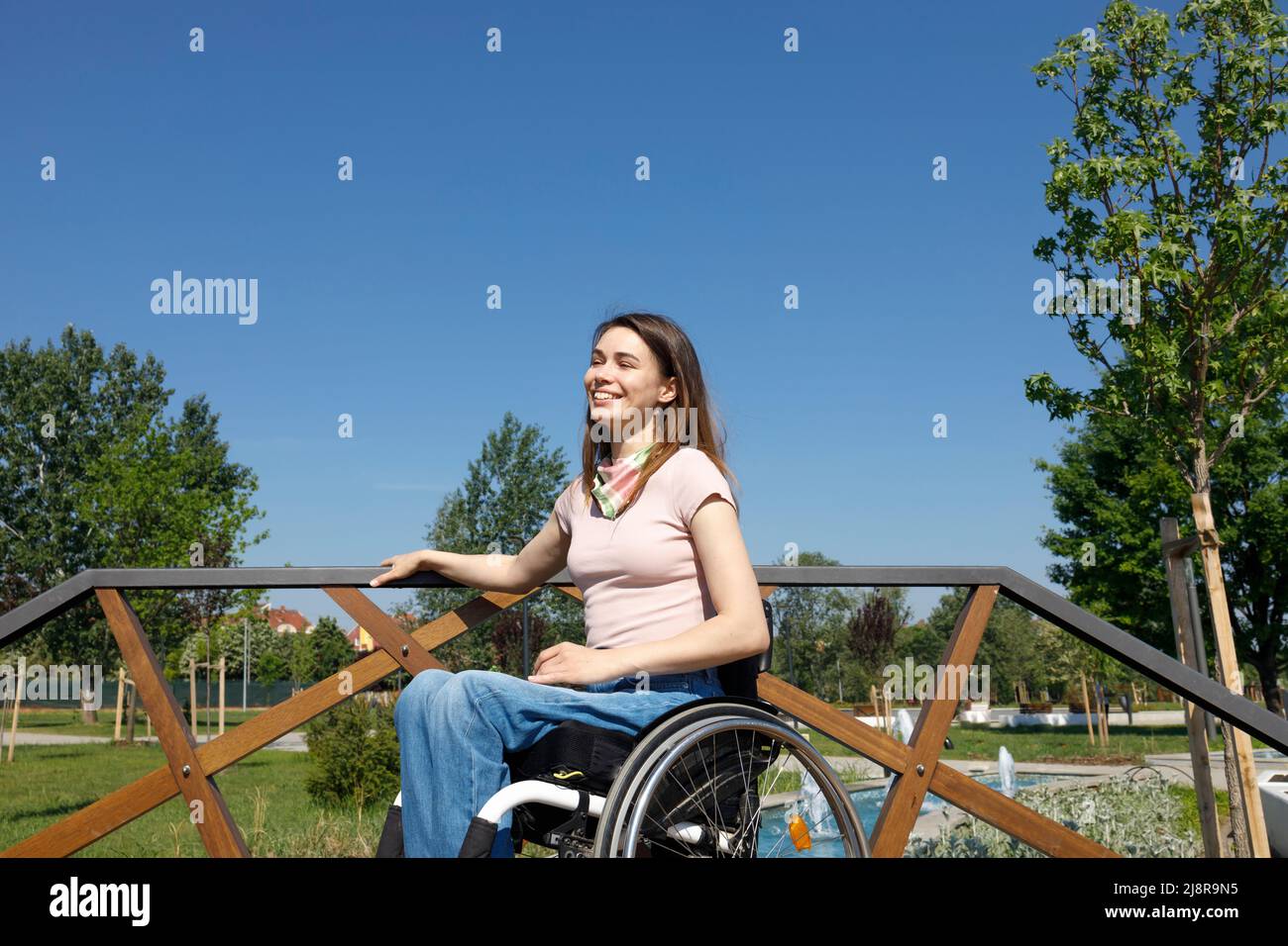 Eine lächelnde Frau, die einen angenehmen Sommertag allein in ihrem Rollstuhl genießt und schätzt Stockfoto