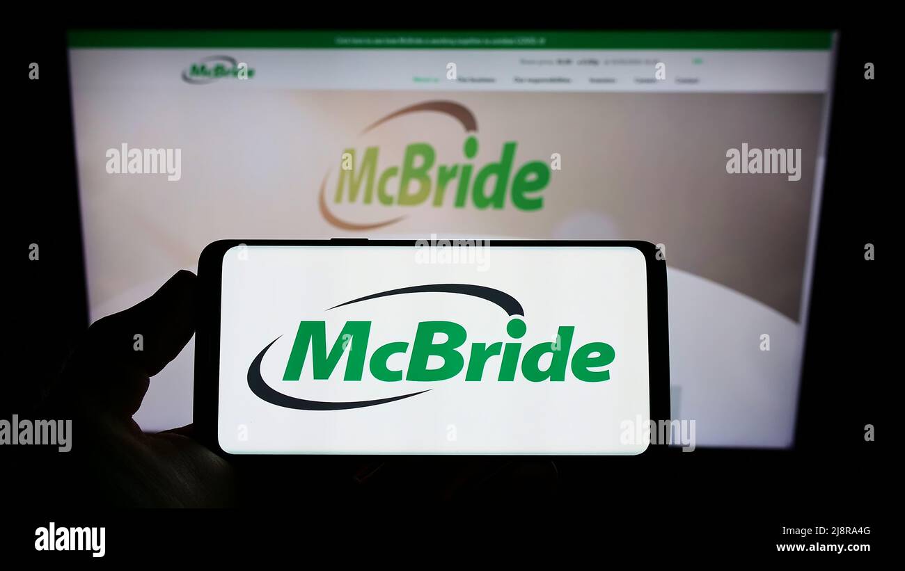 Person, die ein Mobiltelefon mit dem Logo des britischen Haushaltswarenunternehmens McBride plc auf dem Bildschirm vor der Website hält. Konzentrieren Sie sich auf die Telefonanzeige. Stockfoto