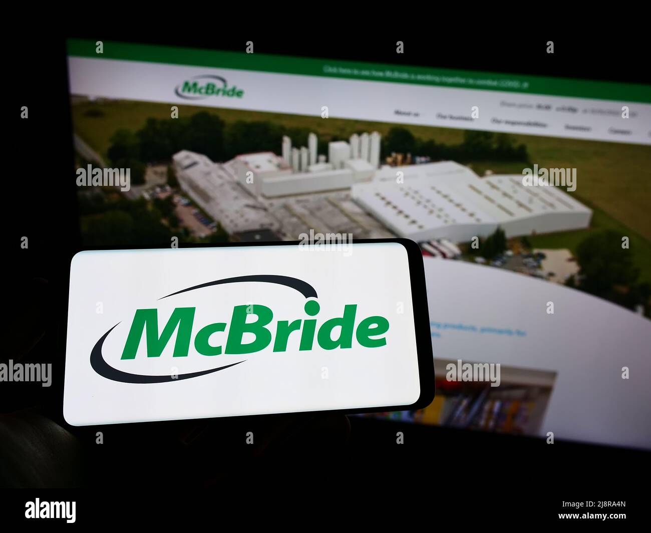 Person, die ein Mobiltelefon mit dem Logo des britischen Haushaltswarenunternehmens McBride plc auf dem Bildschirm vor der Business-Webseite hält. Konzentrieren Sie sich auf die Telefonanzeige. Stockfoto