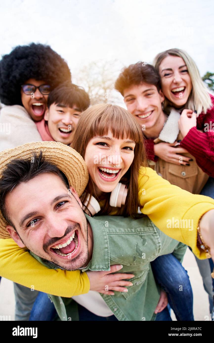 Vertikales Foto einer fröhlichen Gruppe glücklicher Freunde, die ein lächelndes Selfie im Huckepack machen. Drei Paare, die gemeinsam im Park in der Stadt Spaß haben Stockfoto