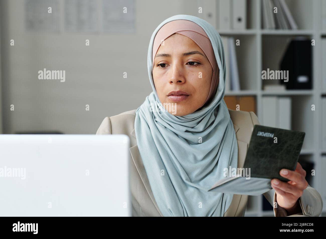 Porträt einer ernsthaften jungen erwachsenen muslimischen Frau mit Hijab, die im Botschaftsbüro sitzt und mit einem Laptop mit Dokumenten arbeitet Stockfoto