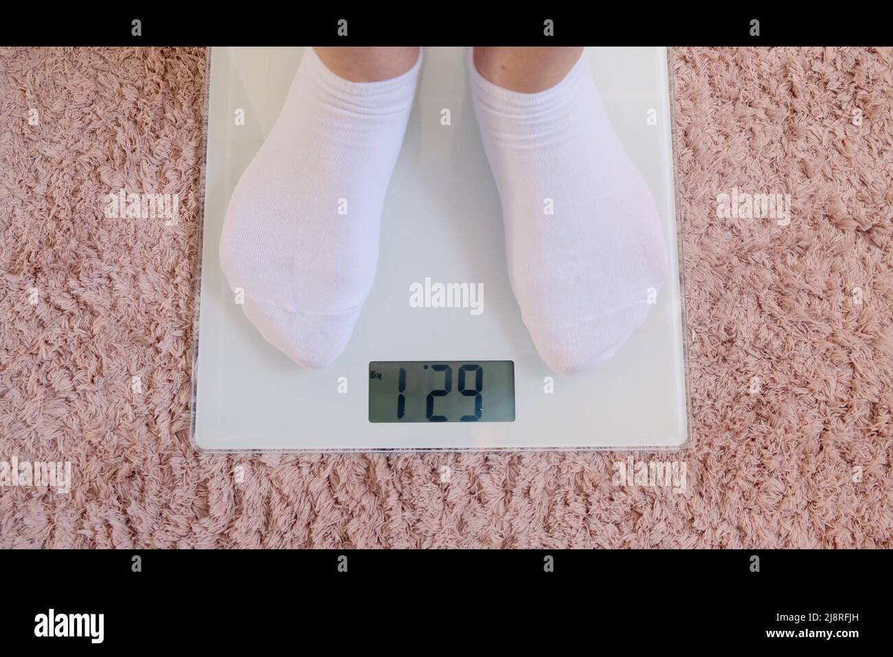 Frauenbeine in weißen Socken stehen auf einer digitalen Waage, um das  Gewicht auf dem Boden im Zimmer zu überprüfen. Schuppen auf rosa Teppich.  Nahaufnahme Stockfotografie - Alamy