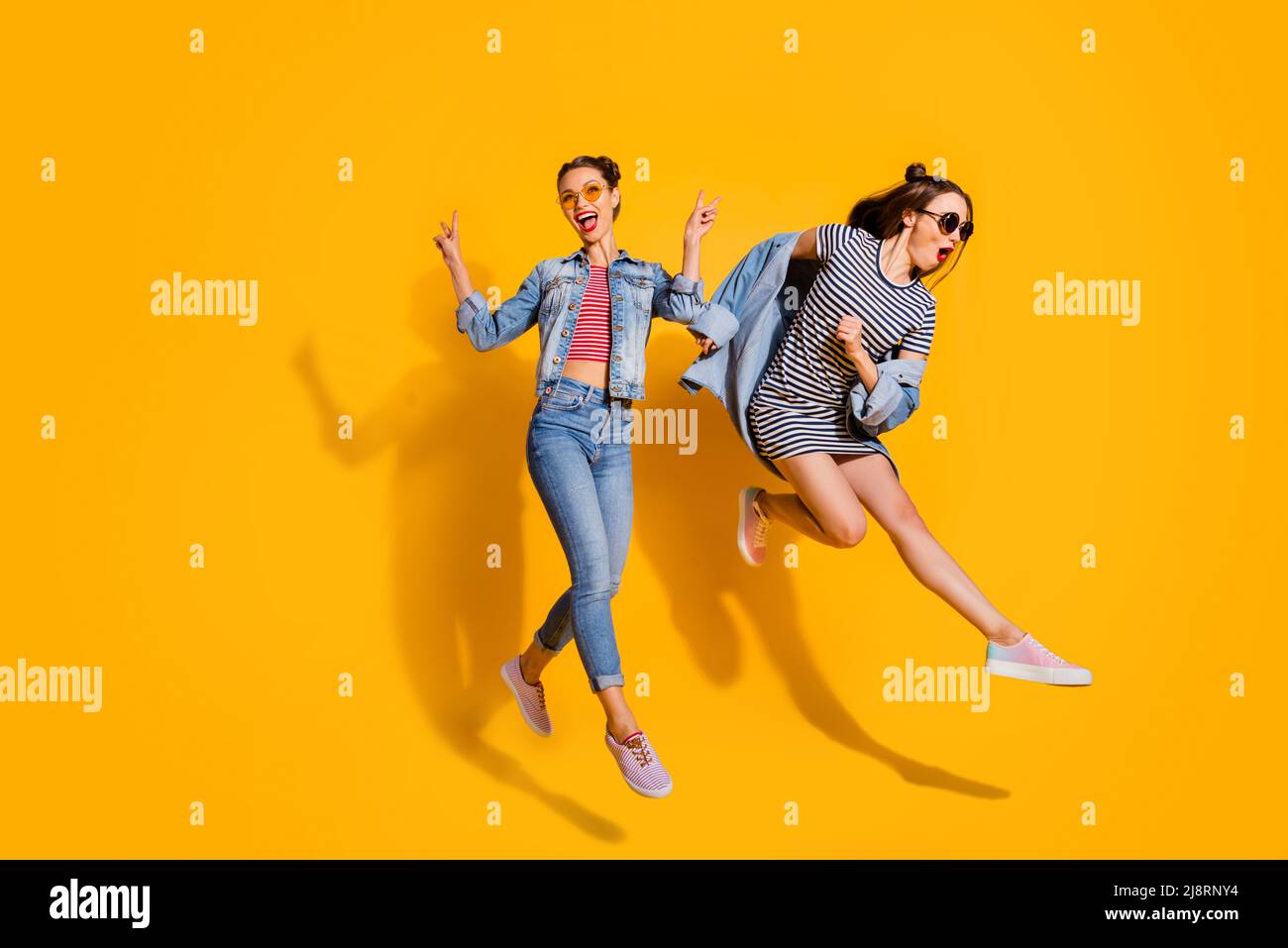 Foto in voller Größe von zwei überglücklich energischen Mädchen springen demonstrieren V-Zeichen isoliert auf gelbem Hintergrund Stockfoto