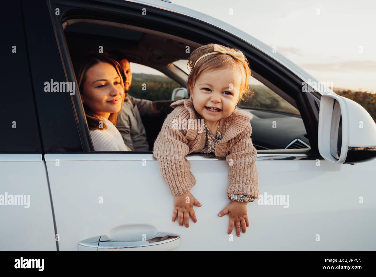 Kleines Mädchen, das aus dem Autofenster schaut, junge Familie mit Baby-Tochter auf einem Roadtrip bei Sonnenuntergang Stockfoto