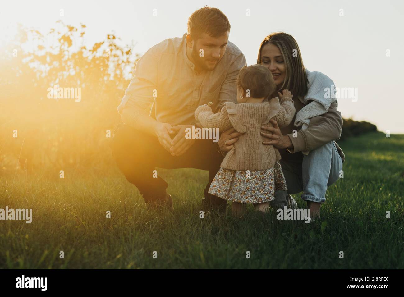 Porträt einer glücklichen jungen kaukasischen Familie, Mutter und Vater mit ihrer kleinen Tochter im Freien bei Sonnenuntergang Stockfoto