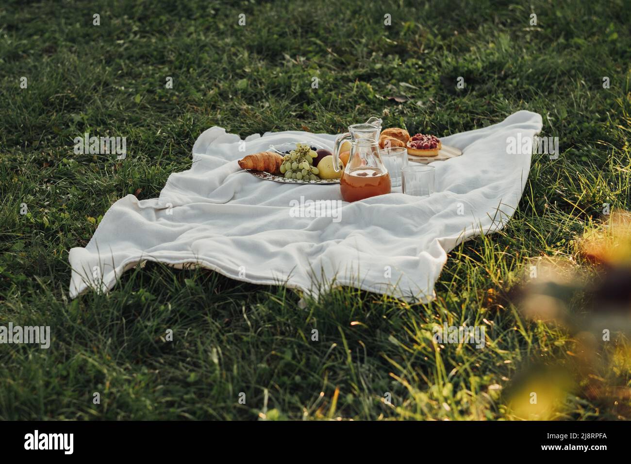 Picknickset auf einem Plaid Outdoor bei Sunset on the Green Grass Stockfoto