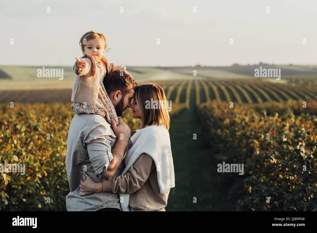 Glückliche junge Familie im Freien, Mutter und Vater mit ihrer kleinen Tochter bei Sonnenuntergang auf dem Feld Stockfoto