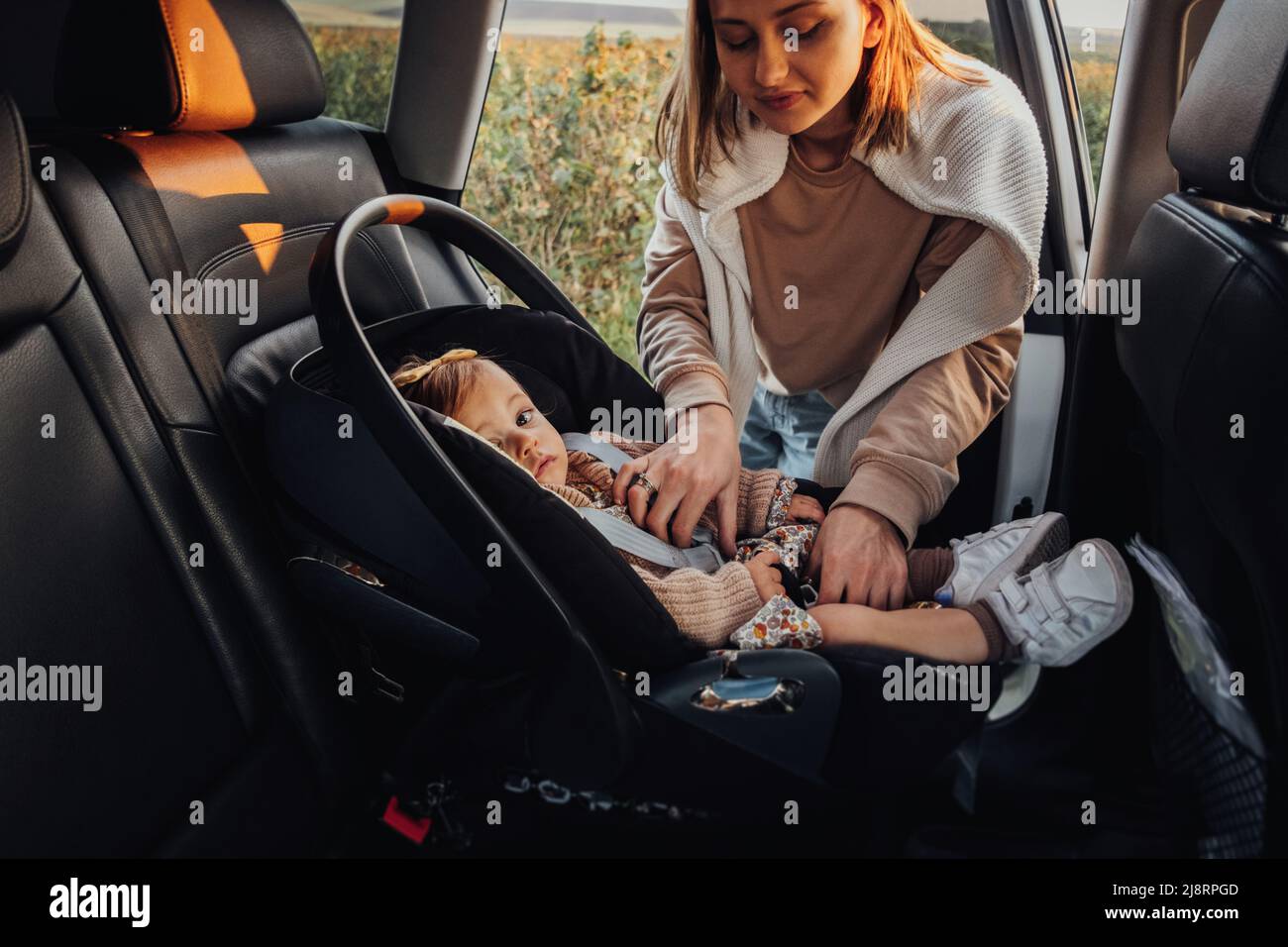 Die junge Mutter legt ihre kleine Tochter auf einen Kinderautositz im Auto Stockfoto