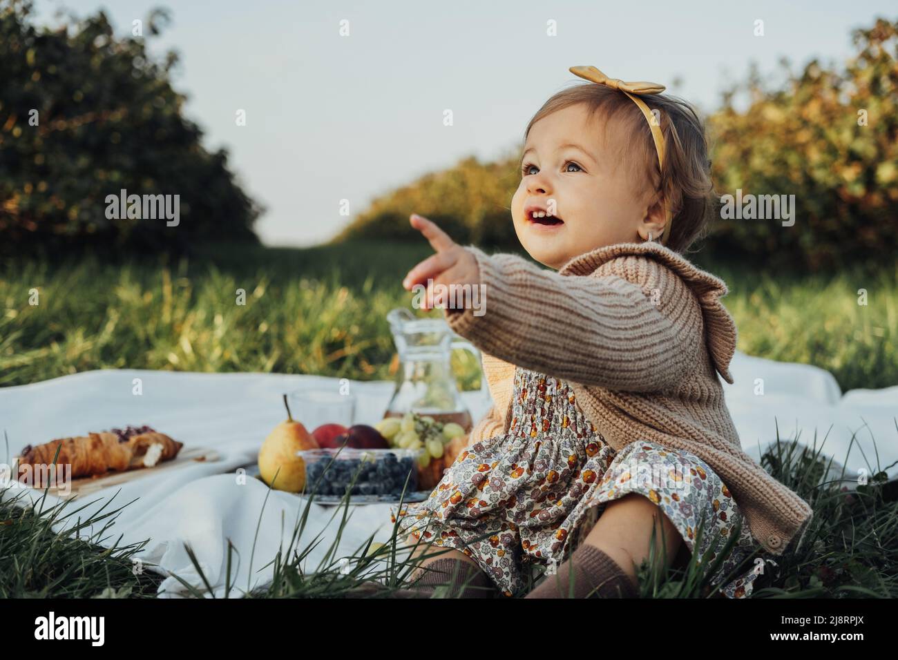 Porträt eines kleinen Mädchens, das auf einem Plaid auf einem Picknick im Freien bei Sonnenuntergang sitzt Stockfoto