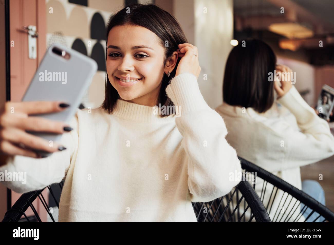 Junge Frau, die Smartphone benutzt und Selfie macht, während sie auf der Couch im Flur des Schönheitssalons sitzt Stockfoto