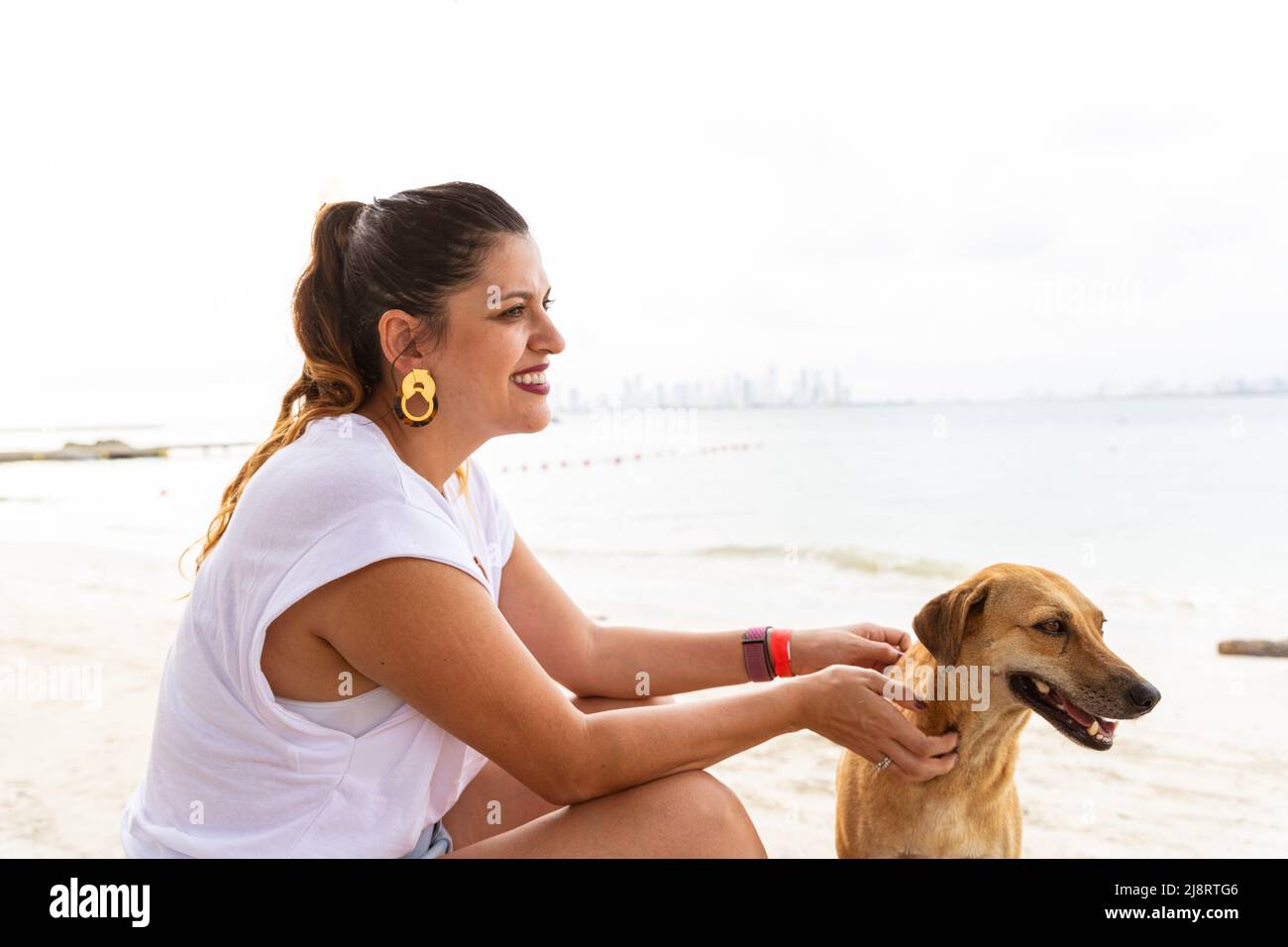 latina-Frau mit ihrem Mischlingshund am Strand Stockfoto