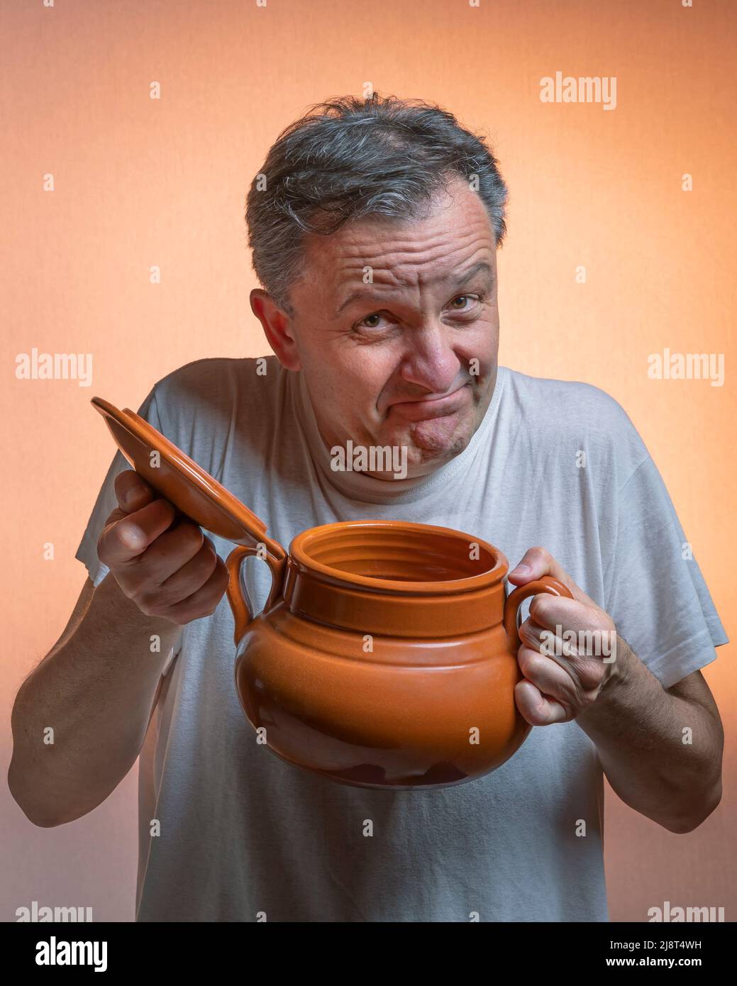 Ein Mann mit einem Tontopf in der einen Hand und dem Deckel in der anderen Hand macht ein lustiges Gesicht Stockfoto