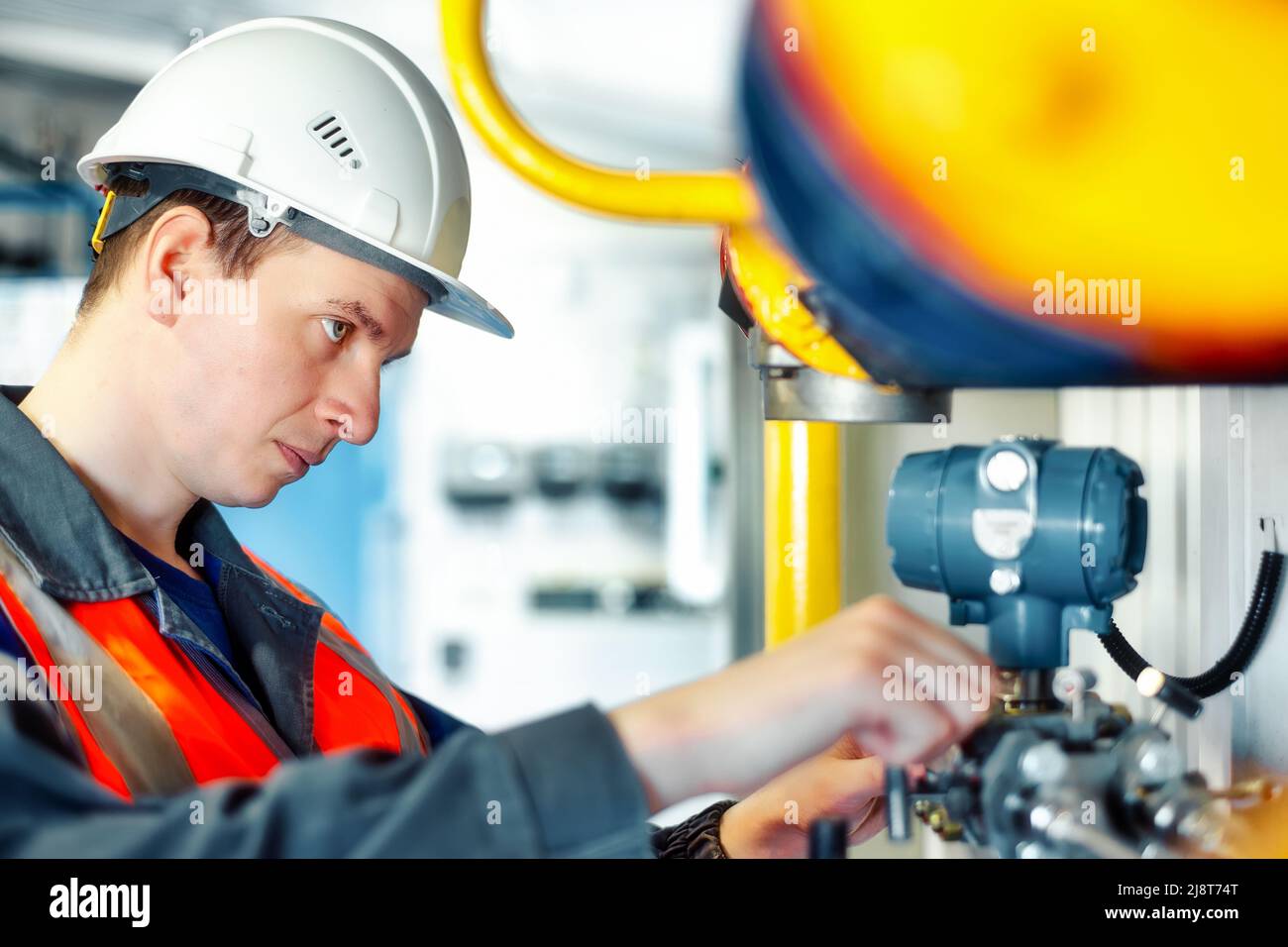 Ein Industrieingenieur im Helm überprüft oder justiert Geräte in einer Gasverarbeitungsanlage oder -Anlage. Authentischer Szenenablauf. Stockfoto