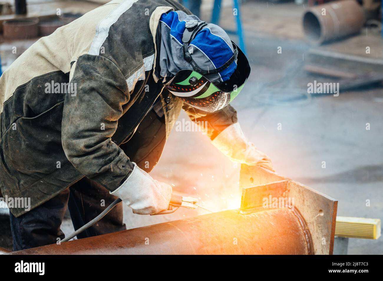 Professioneller Schweißer in Schutzuniform und Maske arbeitet in der Produktionshalle. Authentischer Workflow. Schweißer arbeitet mit Metall und Funken fliegen. Stockfoto