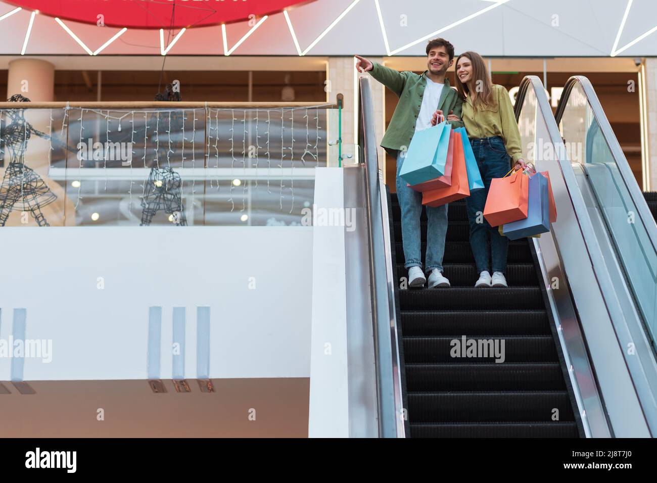 Fröhliches Paar, Das Auf Einer Beweglichen Treppe In Der Modernen Mall Steht Stockfoto