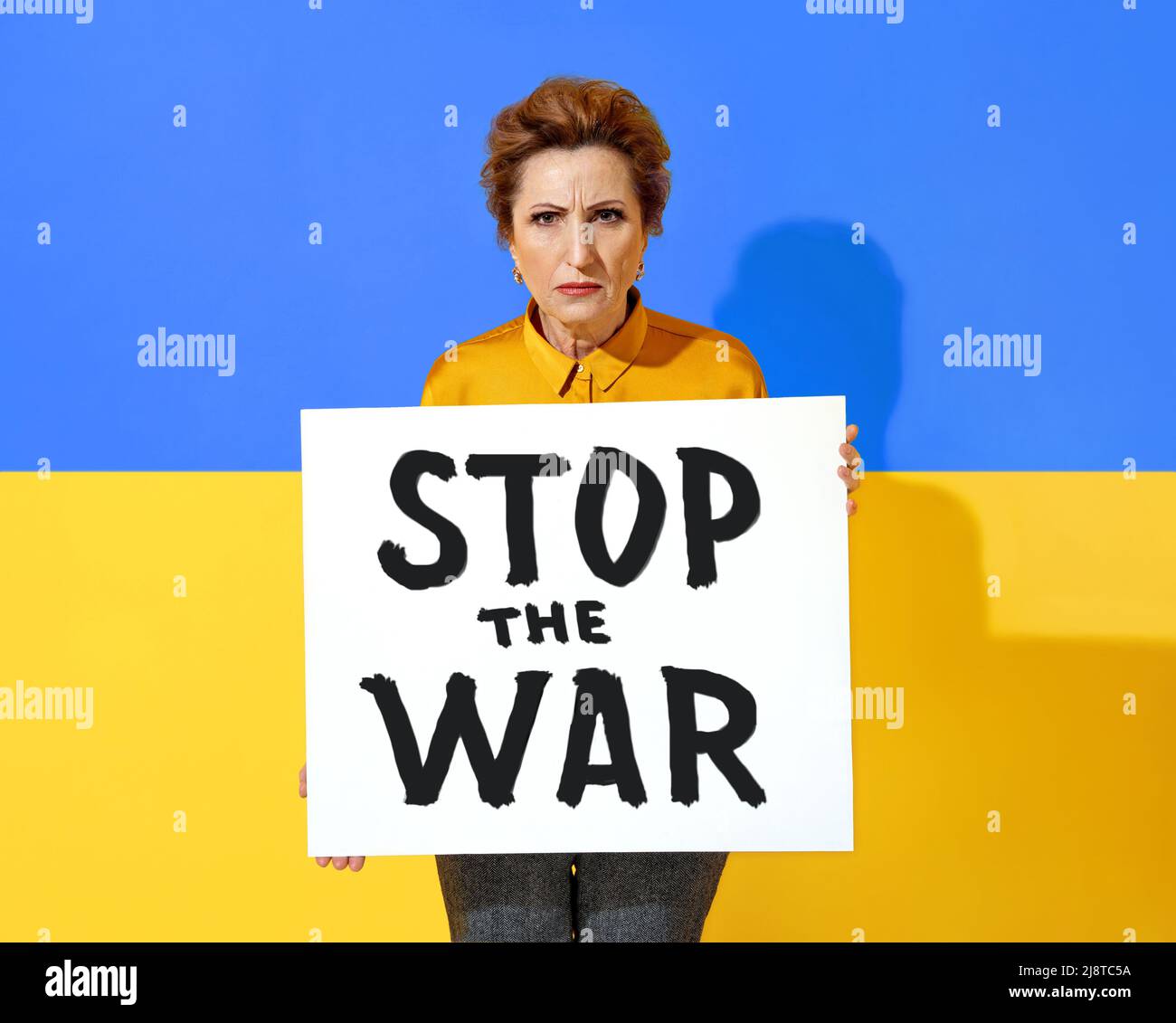 Die ukrainische Frau hält ein Plakat mit der Aufschrift „STOPPEN SIE DEN KRIEG“ vor dem Hintergrund der ukrainischen Flagge Stockfoto
