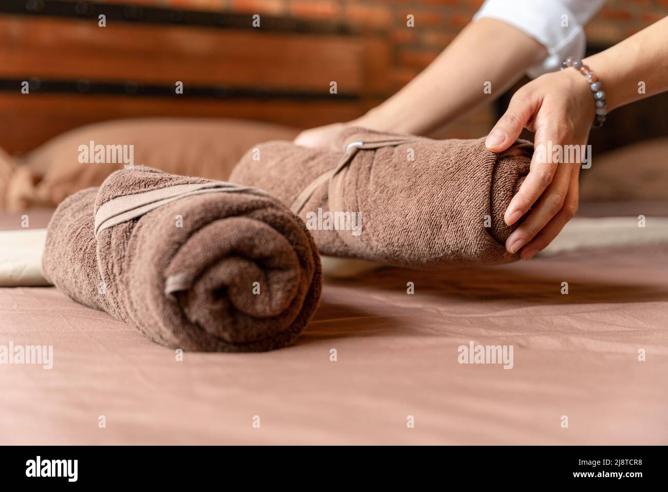 Die Hand des Hotelmadchens, das das Bett mit sauberen, frischen Handtüchern in einem braunen Ziegelsteinzimmer machte. Stockfoto
