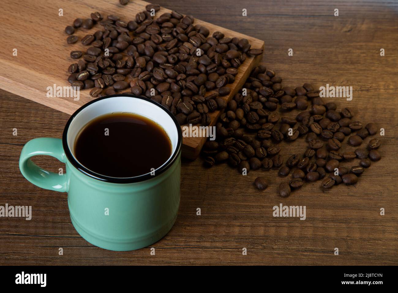 Grüne Tasse Kaffee mit Kaffeebohnen auf Holzhintergrund Stockfoto