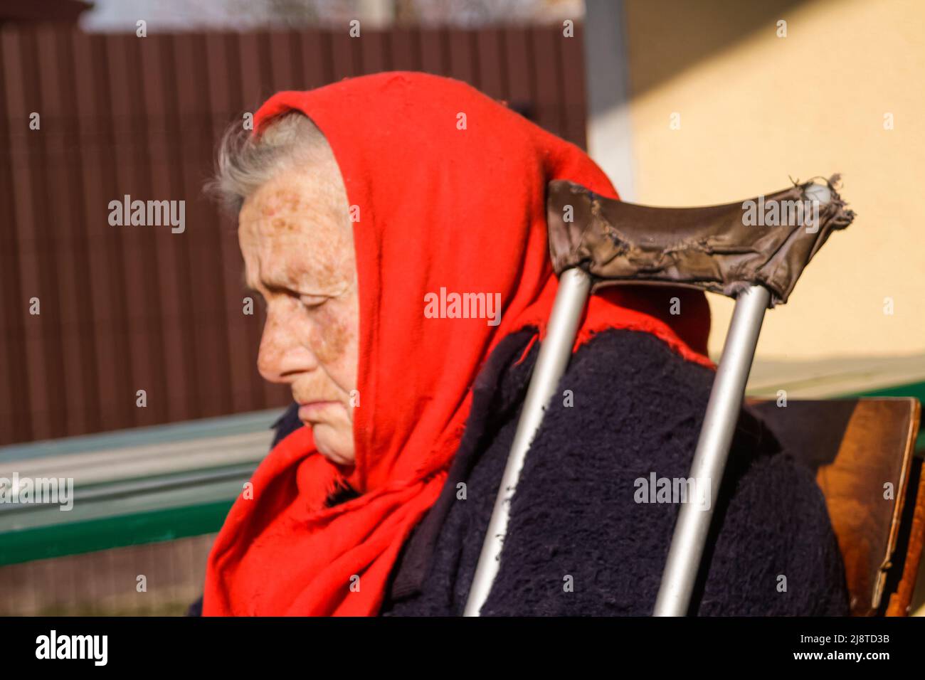 Defokussieren sie die ältere ukrainische Frau in einem roten Schal mit Krücken, die draußen sitzen. Frau 85 Jahre alt. Einzelperson. Nahaufnahme. Verschwommen. Traurige Menschen. Demen Stockfoto