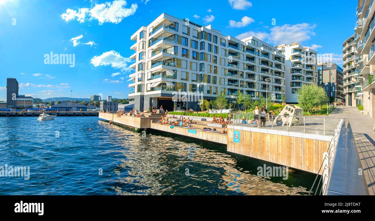 Norweger entspannen und sonnen sich am Ufer von Aker Brygge an einem sonnigen, warmen Tag im Hafen von Oslo. Oslo, Norwegen Stockfoto