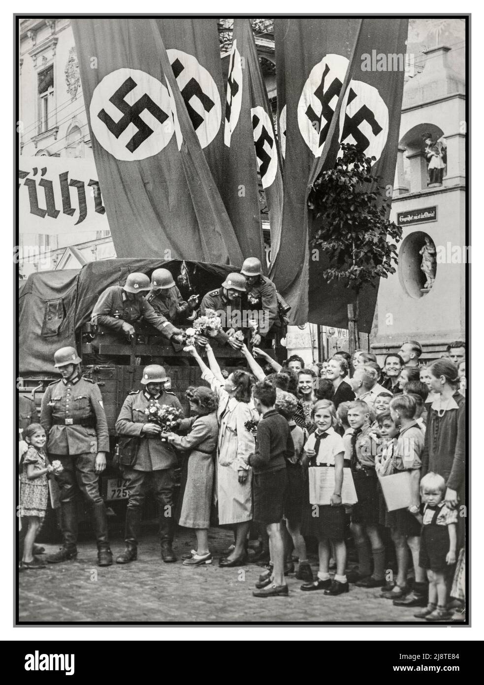 DANZIGER BESETZUNG WW2 Nazi-Propaganda die nazideutschen Truppen in einem aufgesetzten Bild werden nach ihrer ‘Befreiung’ von Danzig mit Blumen begrüßt. Am 1. September 1939 marschierte Hitler in Polen ein, Danzig (laut den Deutschen eine "deutsche" Stadt) war eine der ersten, die besetzt wurde. Polen überreichen in einer organisierten Gruppe Blumen an die Besatzungstruppen der Wehrmacht in Danzig-Polen mit einer Präsentation großer Swastika-Banner dahinter für Fotopropaganda Stockfoto