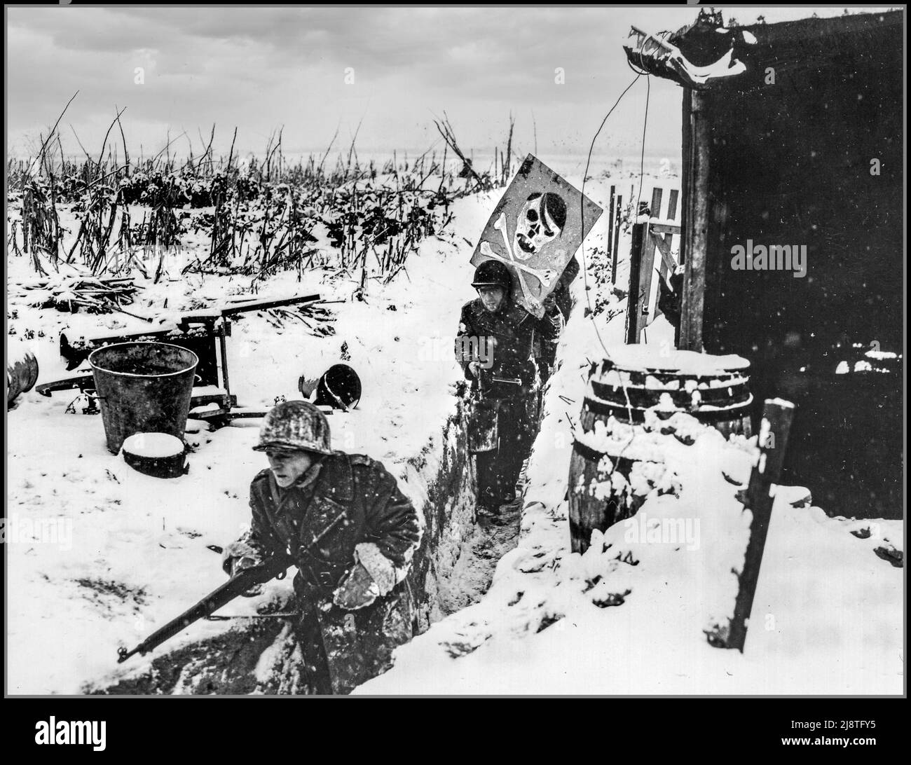 WW2 Rhein Deutschland 1945 Freie französische Infanterie-Patrouille der französischen Armee von 1. trägt ein Karikaturenplakat Hitlers von ihrer schneebedeckten Winterlage am Rhein weg. Das Grabenhumorplakat war auf einem Ufer des Flusses ausgestellt. Nazi-deutsche Beobachter sahen es mit einem Fernglas und durchlösten die Karte wütend mit Kugeln. 5 Januar 1945. Huningue, Frankreich. Fotograf: Stubenrauch. Stockfoto