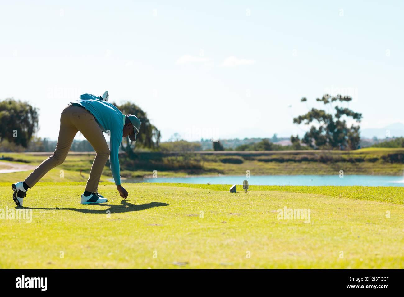 Der ganze afroamerikanische junge Mann hält einen Schläger, der den Golfball auf dem Abschlag auf dem Golfplatz platziert Stockfoto