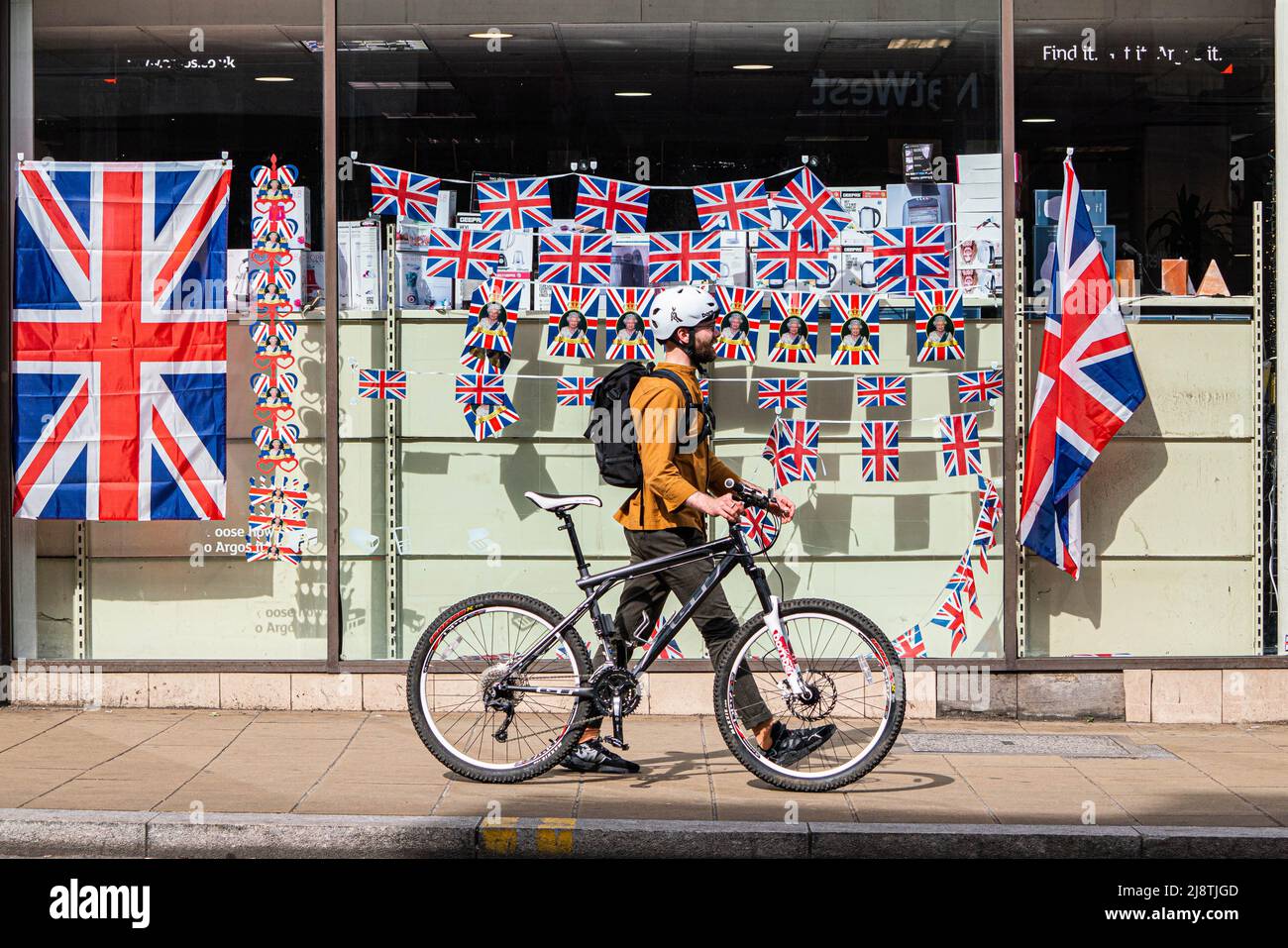 London, 18. Mai 2022. Eine Fußgängerin geht an einem Schaufenster im Stadtzentrum von Wimbledon vorbei, das mit Union Jack-Fahnen geschmückt ist und das Platinjubiläum feiert, da Königin Elizabeth 70 Jahre als die am längsten dienende britische Monarchie seit ihrer Thronbesteigung im Jahr 1952 feiert. Kredit. amer Ghazzal/Alamy Live Nachrichten Stockfoto