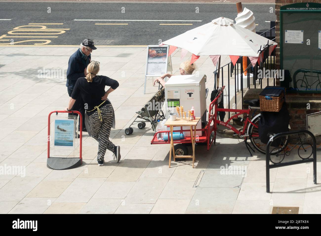 Mann, der mit der Eisdiele der Frau plaudert, die in Northallerton North Yorkshire einen traditionellen Dreirad-Pedalwagen hat Stockfoto