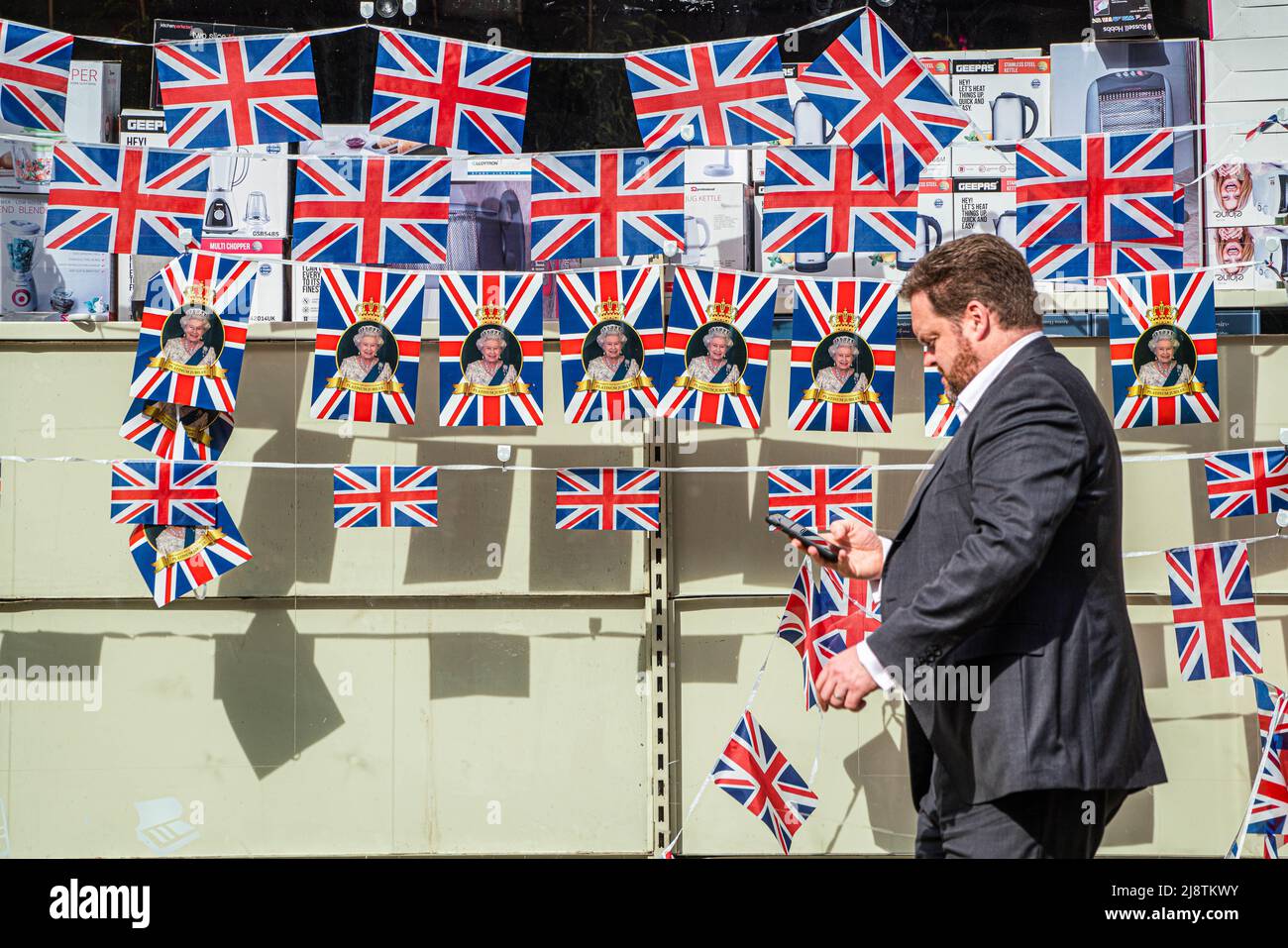 London, 18. Mai 2022. Eine Fußgängerin geht an einem Schaufenster im Stadtzentrum von Wimbledon vorbei, das mit Union Jack-Fahnen geschmückt ist und das Platinjubiläum feiert, da Königin Elizabeth 70 Jahre als die am längsten dienende britische Monarchie seit ihrer Thronbesteigung im Jahr 1952 feiert. Kredit. amer Ghazzal/Alamy Live Nachrichten Stockfoto